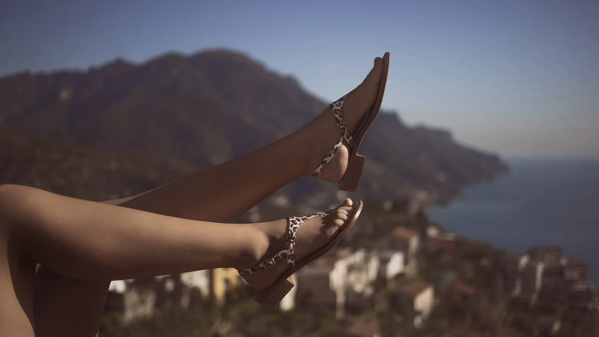 Gambe sollevate con sandali di cuoio, sullo sfondo Ravello e la costa